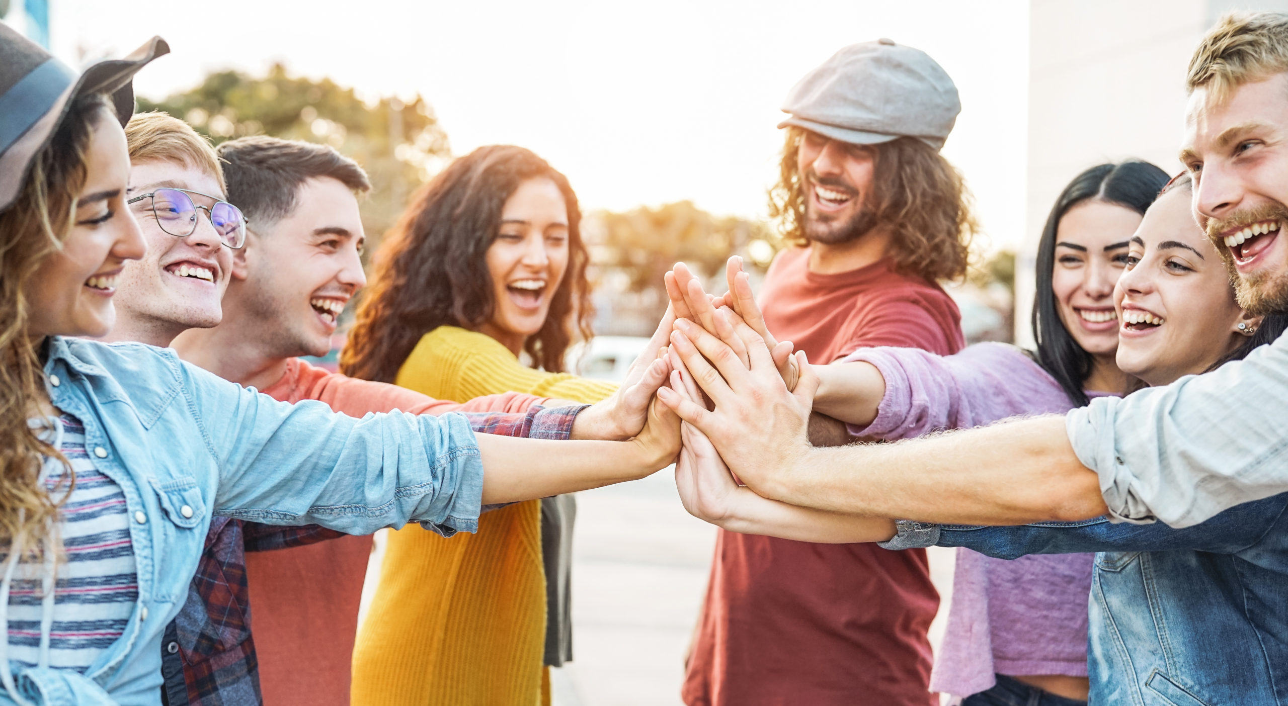 Young friends stacking hands outdoor – Happy millennial people having fun joining and celebrating together – Friendship, empowering, teamwork, partnership and youth lifestyle concept